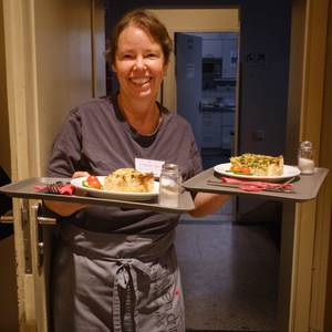 Frau kommt mit zwei Tablets mit Quiche aus der Tür