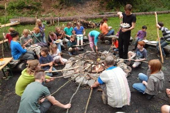 Kinder sitzen um ein Lagerfeuer und machen Stockbrot